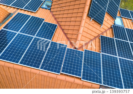 Aerial top view of new modern residential house cottage with blue shiny solar photo voltaic panels system on roof. Renewable ecological green energy production concept. Aerial top view of new modern residential house cottage with blue shiny solar photo voltaic panels system on roof. Renewable ecological green energy production concept. 139393757