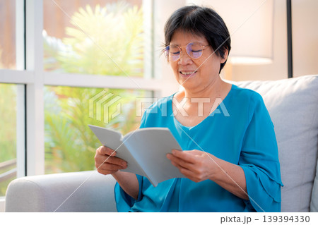 Asian senior woman reading a book sitting on sofa with relax in living room at home. 139394330