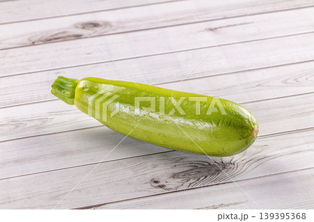 Single fresh green zucchini with water droplets on a light wooden background. Single fresh green zucchini with water droplets on a light wooden background. 139395368