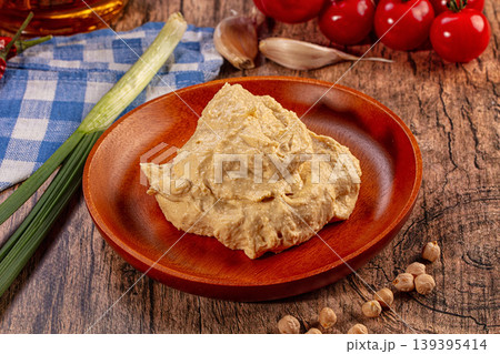 Creamy hummus on wooden plate with fresh ingredients, chickpeas, tomatoes, garlic, green onion, olive oil 139395414
