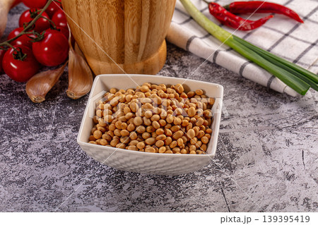 Soybeans in white bowl with fresh cherry tomatoes, garlic, chili peppers, green onions on textured surface 139395419