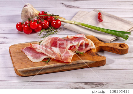 Delicate raw bacon slices, fresh rosemary, cherry tomatoes, garlic, green onion, chili pepper on rustic wooden board 139395435