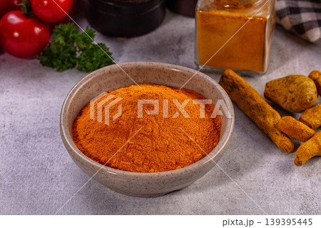 Bright orange turmeric powder in ceramic bowl, fresh red tomatoes, green parsley, whole roots, spice jar on grey surface Bright orange turmeric powder in ceramic bowl, fresh red tomatoes, green parsley, whole roots, spice jar on grey surface 139395445