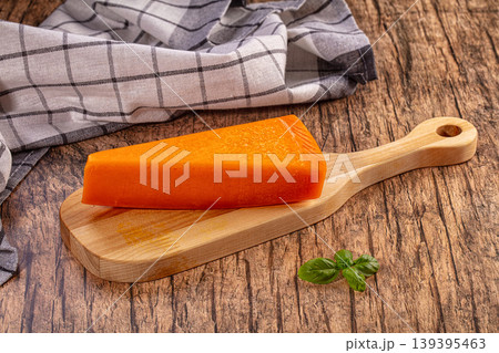 Orange cheese wedge on wooden cutting board, rustic background, fresh basil leaves Orange cheese wedge on wooden cutting board, rustic background, fresh basil leaves 139395463