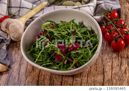 Fresh green arugula radicchio salad in bowl with cherry tomatoes garlic on rustic wood 139395465