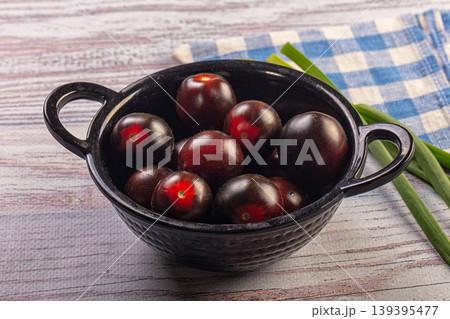Ripe black cherry tomatoes in dark bowl with scallions on rustic wood background 139395477