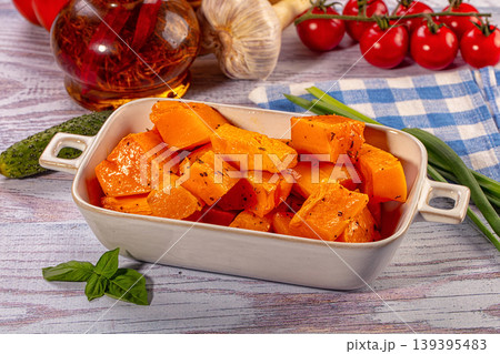 Roasted butternut squash with herbs in ceramic dish surrounded by fresh vegetables 139395483