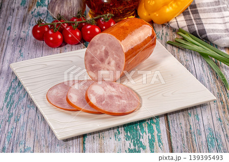 Sliced boiled ham sausage on white plate with fresh vegetables on rustic wooden table 139395493