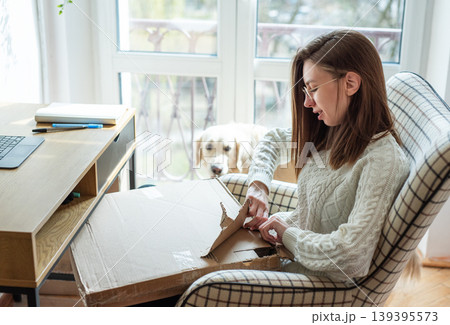 Woman unboxing package at home with dog watching Woman unboxing package at home with dog watching 139395573