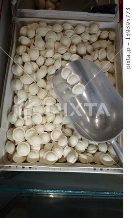 White dumpling wrappers piled in a container with a metal scoop resting on top, showcasing the texture and shape of the uncooked dough pieces 139395773
