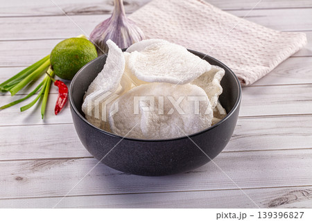 Crispy shrimp chips in a dark bowl with fresh chili, garlic, and lime ingredients on a white wooden background. Crispy shrimp chips in a dark bowl with fresh chili, garlic, and lime ingredients on a white wooden background. 139396827
