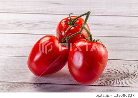 Fresh ripe red tomatoes on a vine resting on a light wooden background. Fresh ripe red tomatoes on a vine resting on a light wooden background. 139396837