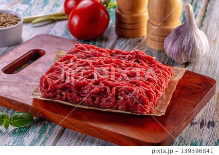 Raw ground beef on a wooden cutting board with fresh tomatoes, garlic, and spices. Raw ground beef on a wooden cutting board with fresh tomatoes, garlic, and spices. 139396841
