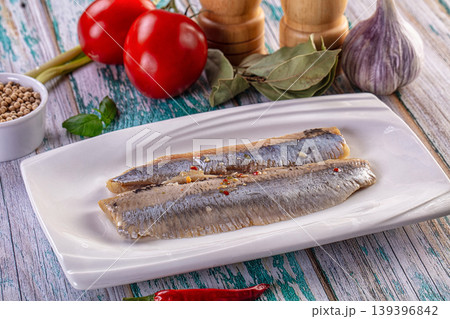 Salted herring fillets on a plate with fresh tomatoes, garlic, chili, and spices on a rustic wooden background. Salted herring fillets on a plate with fresh tomatoes, garlic, chili, and spices on a rustic wooden background. 139396842