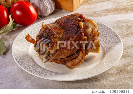 Roasted pork knuckle with crispy skin served on a plate with fresh tomatoes and garlic on a wooden table Roasted pork knuckle with crispy skin served on a plate with fresh tomatoes and garlic on a wooden table 139396851