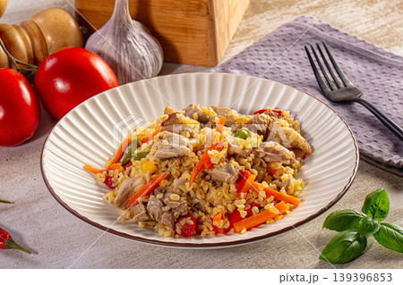 Hearty pilaf with meat and vegetables on a plate surrounded by fresh ingredients 139396853