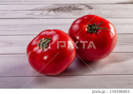 Close up of two organic red tomatoes with green stems on a rustic wood surface Close up of two organic red tomatoes with green stems on a rustic wood surface 139396863
