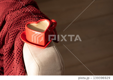 Heart Shaped Coffee Cup on Armchair with Red Blanket. Heart Shaped Coffee Cup on Armchair with Red Blanket. 139396929