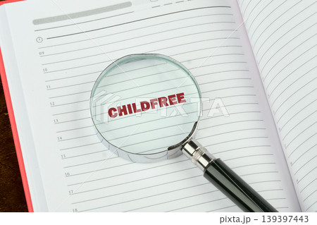 A magnifying glass rests on an open planner, clearly showing the red word CHILDFREE on a lined page with hourly entries and time slots A magnifying glass rests on an open planner, clearly showing the red word CHILDFREE on a lined page with hourly entries and time slots 139397443