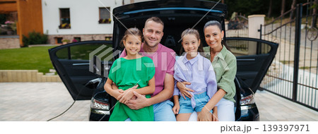 Happy family sitting in car trunk and waiting for electric car charging. Happy family sitting in car trunk and waiting for electric car charging. 139397971