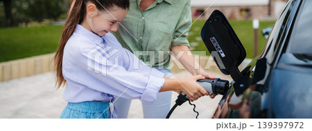 Mother and girl charging electric car while family prepares for summer trip. 139397972