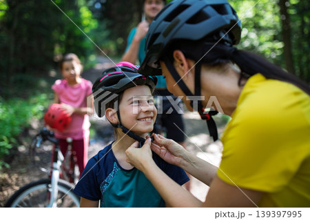 Mother fastening helmet on daughter before cycling for safety. Mother fastening helmet on daughter before cycling for safety. 139397995