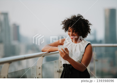 Portrait of a businesswoman standing on a terrace of modern office, scrolling on phone. 139398096