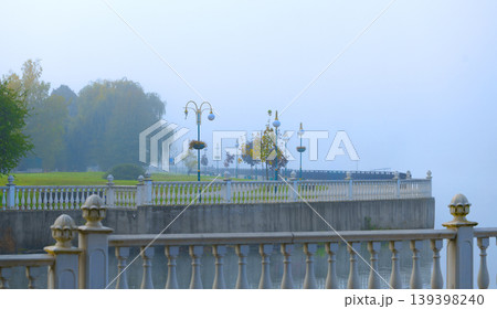 Misty waterfront promenade with ornate railings and vintage lampposts on a serene river side Misty waterfront promenade with ornate railings and vintage lampposts on a serene river side 139398240