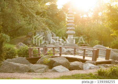 Majestic sun shines on a tranquil Asian park with a pagoda and wooden bridge 139398255