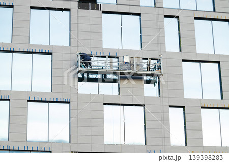 Workers on a suspended platform installing facade panels on a modern skyscraper 139398283