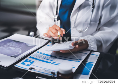 Two doctors and a female nurse meet at a table in the hospital, collaborating on medical tasks using laptops and computers Two doctors and a female nurse meet at a table in the hospital, collaborating on medical tasks using laptops and computers 139398534