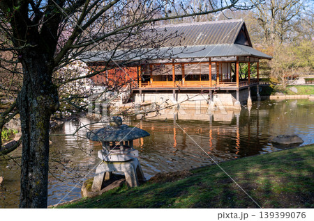 Tranquil waterside pavilion featuring lush blossoms surrounding traditional Japanese garden scene 139399076