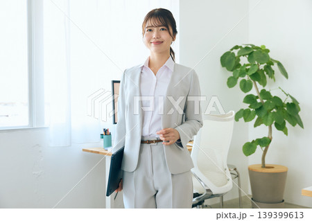 オフィスでタブレットを持ち微笑む若い女性ビジネスパーソン・グレーのスーツ姿の会社員 139399613