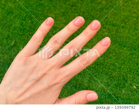 Woman hand with fresh well groomed manicure of natural tone, short nails on green grass background. Beauty routine and care, decorative for design, spa and relax 139399792