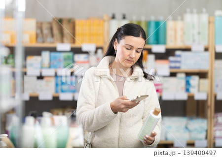 Middle-aged woman scanning QR-code on shampoo in drugstore Middle-aged woman scanning QR-code on shampoo in drugstore 139400497