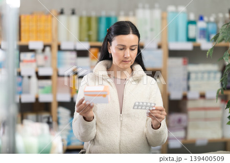 Middle-aged woman customer holding pills with box in drugstore 139400509