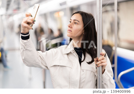 In the subway car, woman with mobile phone makes a selfie or scans QR code In the subway car, woman with mobile phone makes a selfie or scans QR code 139400996