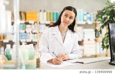 Female pharmacist working at computer and filling out papers 139400998