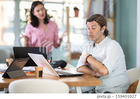 Woman scolding sad colleague sitting at laptop in office Woman scolding sad colleague sitting at laptop in office 139401027