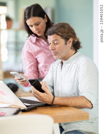 Middle-aged male and female colleagues looking at smartphone at office 139401052