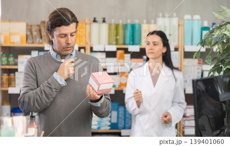 Middle-aged man choosing pills in box while pharmacist offering in drugstore Middle-aged man choosing pills in box while pharmacist offering in drugstore 139401060
