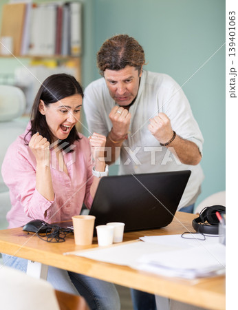 Happy colleagues sharing success while looking at laptop screen Happy colleagues sharing success while looking at laptop screen 139401063