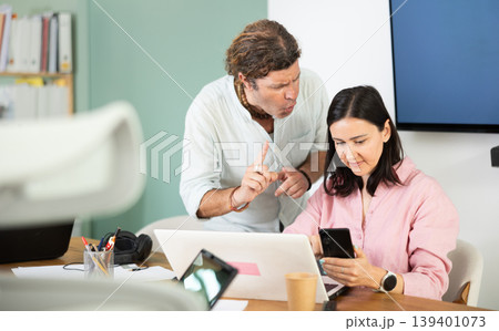 Businessman complains to subordinate about her talking on her mobile phone while working in office 139401073