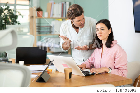 Young businessman of large company, scolds his employee girl sitting at workdesk in office Young businessman of large company, scolds his employee girl sitting at workdesk in office 139401093