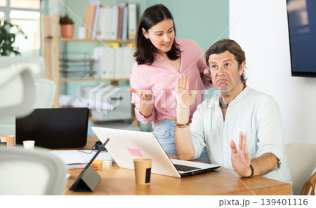 Adult woman scolding adult male colleague working on laptop Adult woman scolding adult male colleague working on laptop 139401116