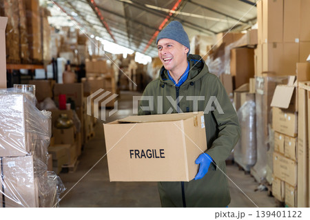 Positive worker carrying cardboard box with fragile content 139401122