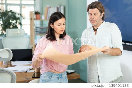 Middle-aged man and woman discussing construction plan standing in office 139401128