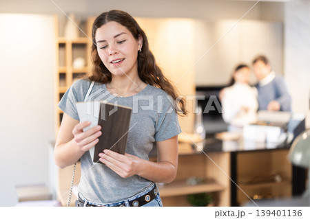 Female buyer with samples of material chooses kitchen set in furniture store 139401136