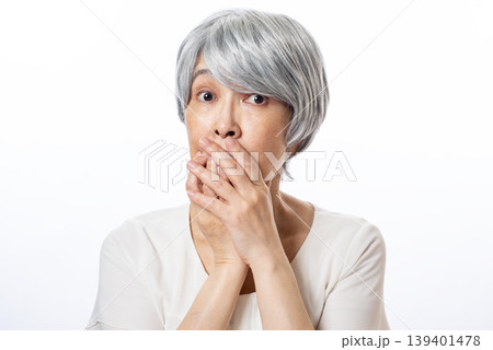 口元を両手で隠し目を見開き驚いた表情のシニア女性 口元を両手で隠し目を見開き驚いた表情のシニア女性 139401478