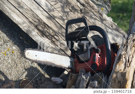 Close-up of a red chainsaw resting on weathered wood and rocks Close-up of a red chainsaw resting on weathered wood and rocks 139401718
